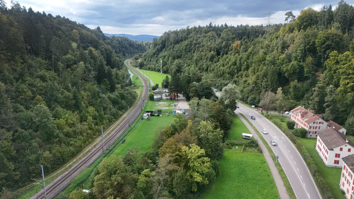 Noch schlängelt sich die Bahn auf einer Spur durchs Aatal. Luftbild des Aatals mit Bahnlinie und Strasse sowie der ehemaligen Arbeitersiedlung in Unteraathal.